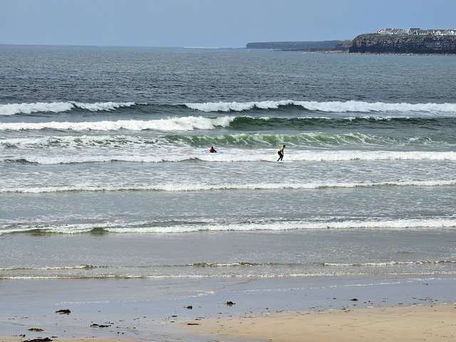 2 foot waves breaking on the main beach with a beginner surfer riding a wave in the shallows
